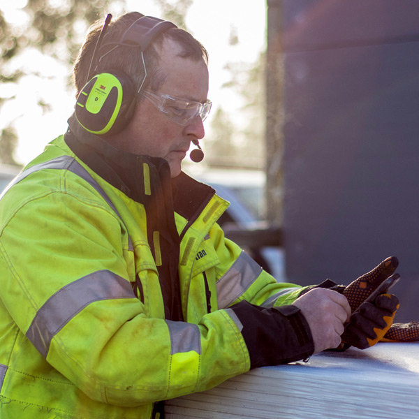 Person i varselkläder med Peltor hörselskydd med mikrofon använder en smartphone.