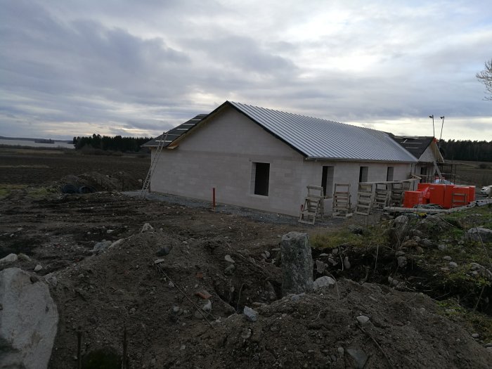 Hus under konstruktion med nylagt plåttak och synliga byggnadsställningar på landsbygden.