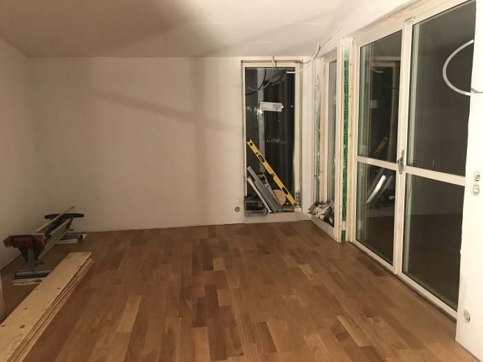 Inredning av ett vardagsrum under renovering med nytt trägolv och ej färdigställda altandörrar.