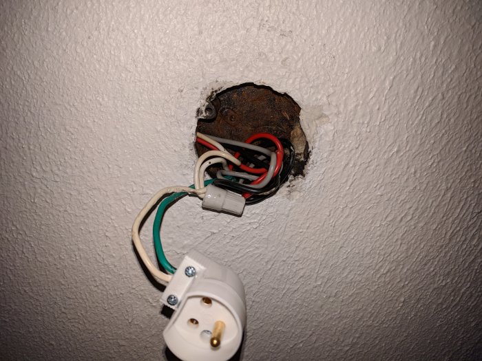 En öppen elektrisk kopplingsdosa utan krok i taket med synliga kablar och en avslutad kabel.