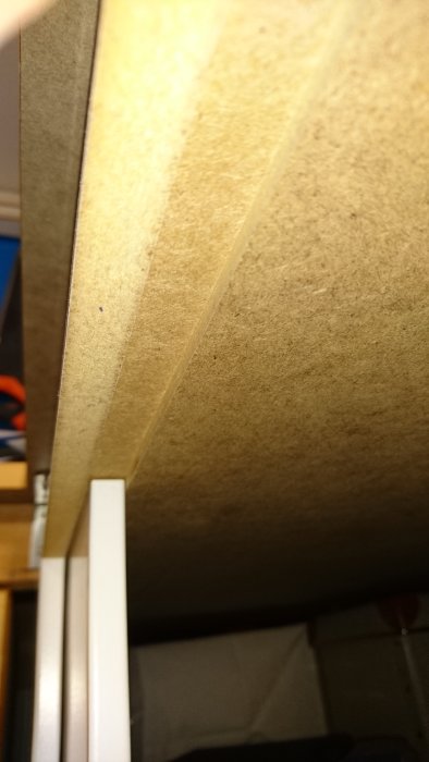 Närplan av ett hemmagjort skåp med MDF-lucka glidande på en vit aluminiumremsa i botten, visar fräst spår och övergång mellan material.