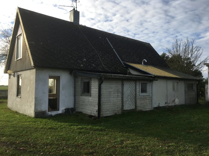 Ett äldre litet hus på landet med tegeltak, delvis sliten vit fasad och träpanel behövande renovering.