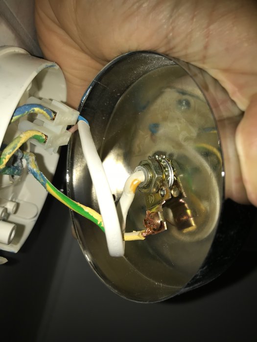 Närbild på en öppen vägglampa med exponerade ledningar och elektriska anslutningar.