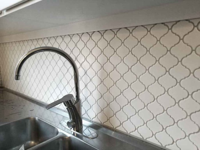 Kakelvägg med vit marockansk mosaik bakom en kökskran, med vissa plattor skurna vid topp och botten.