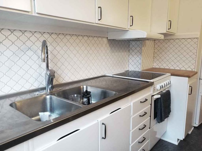Kök med vit mosaikstänkskydd, spis bredvid diskbänk och träbänkskiva, trimmad mosaik övre och nedre kant.