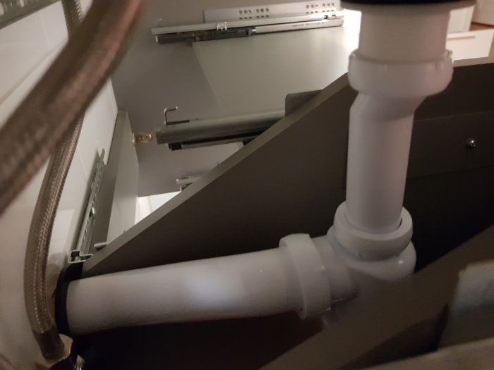 Nyligen installerat 40mm vattenlås och avloppsrör under handfat, syns bakom badrumsskåp.