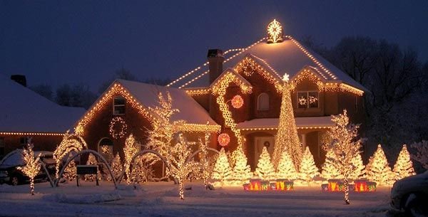 Hus dekorerat med julbelysning på kvällen, snötäckt trädgård och ljusdekorerade träd och buskar.