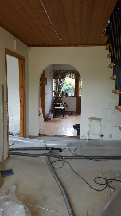 Interiör av hus under renovering med synliga golvreglar, elledningar och träpanel i taket.