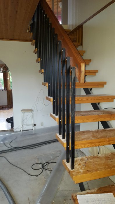 Trappa under renovering med trästeg och svarta vertikala balustrader i ett hus från 1967.