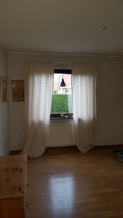 Före renovering: vardagsrum med trägolv, vita gardiner och 60-talsinredning.