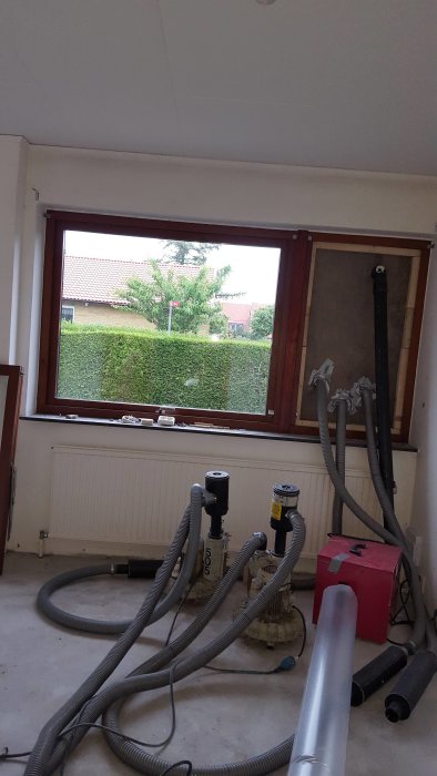 Renoveringsprojekt före-bild av ett rum med byggmaterial och verktyg på golvet framför fönstret.