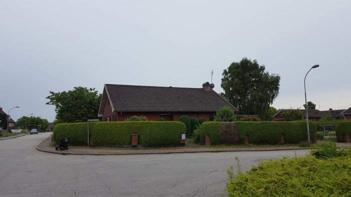 Ett 1,5-plans tegelhus från 1967 före renovering omgivet av en välskött häck och en grå himmel i bakgrunden.