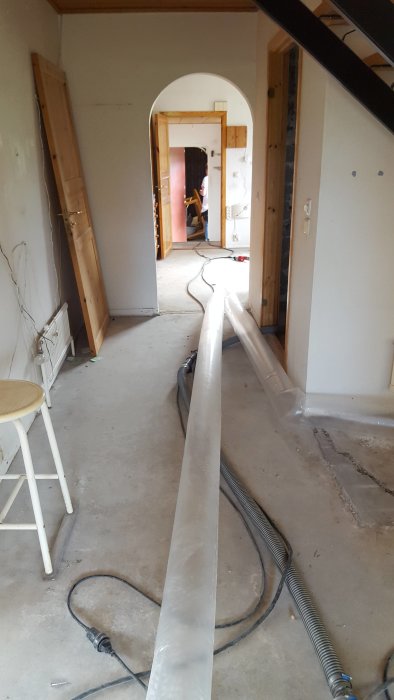 Interiör av ett hus under renovering med avlägsnat golv och synlig elledningar.