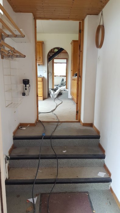 Bild på en renoveringsklar hall i ett hus med trappsteg, trähållare för hattar och ledningar på golvet.