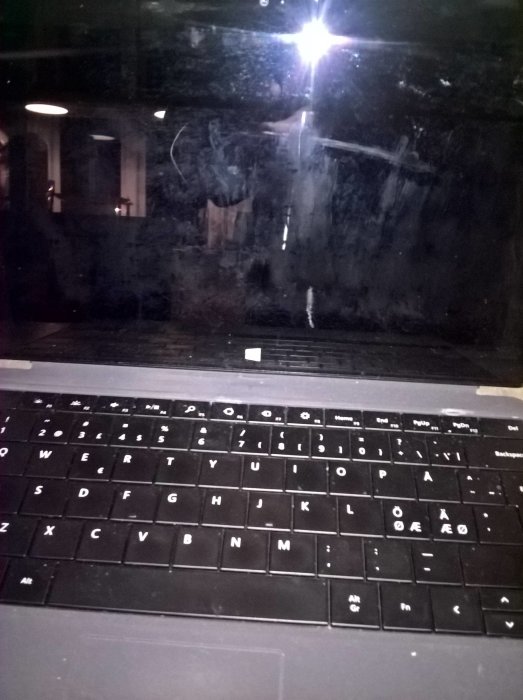 Smutsig laptopskärm som reflekterar ett rum, synligt tangentbord med svenska tecken.