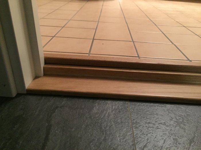 En dörrtröskel mellan två rum med kakelgolv och en laminattröskel som anpassats med silikon.