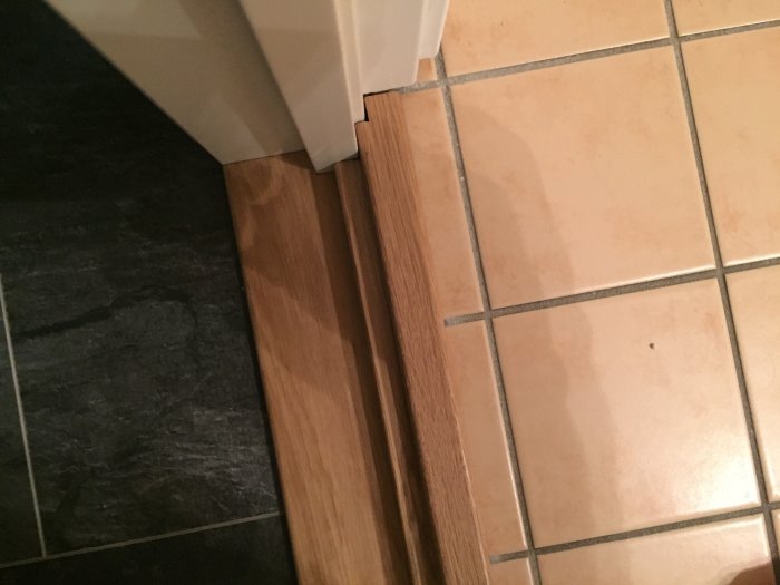 Golvövergång med trälist mellan mörkt och ljust klinkergolv vid dörrpost.