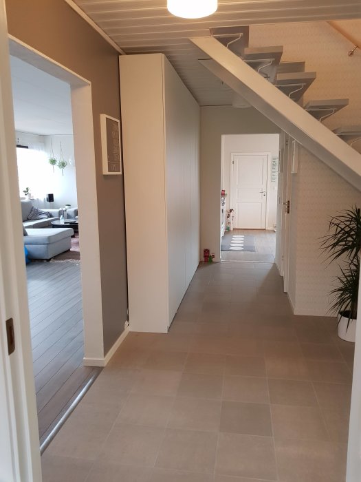 Renoverad entré med grått klinkergolv, vit trapp och inblick i vardagsrum.