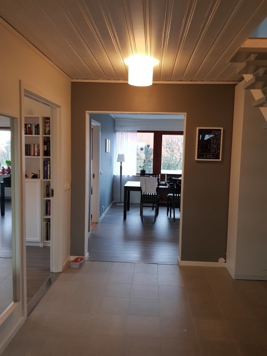 Renoverat interiör med ljusgrått golv, vit taklampa och vitmålade väggar i ett tomt rum med trappa.