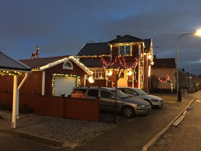 Ett hus dekorerat med julbelysning och renfigurer på taket under skymningen.