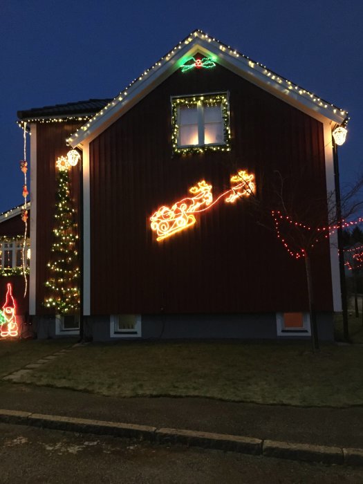 Hus med julbelysning inklusive renar, släde och julgransdekorationer i skymningen.