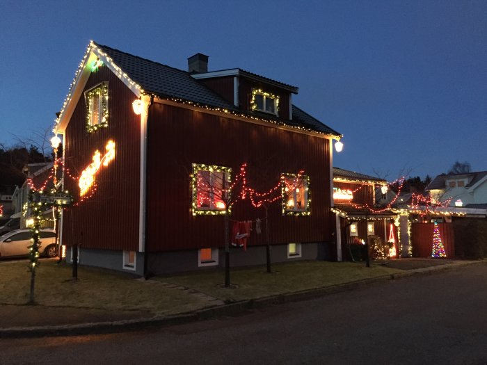 Röd trävilla dekorerad med julbelysning i skymningen.