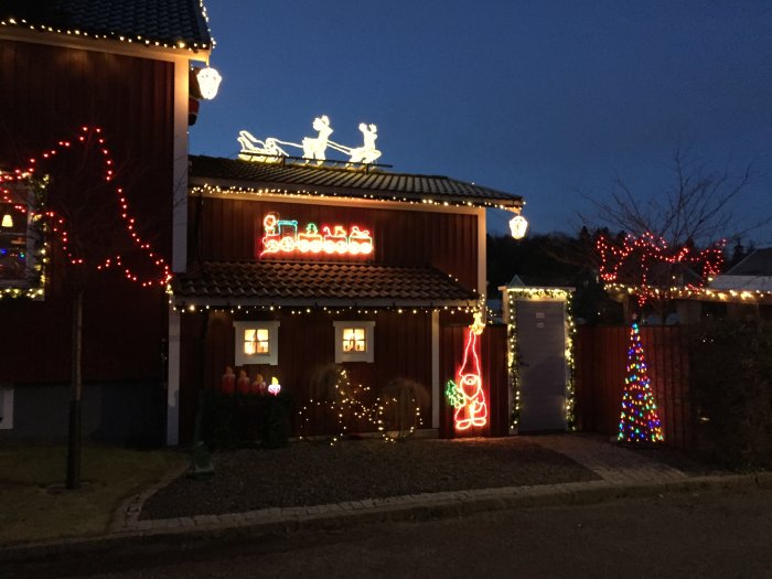 Ett hus dekorerat med julbelysning och figurer, inklusive tomtar och renar.