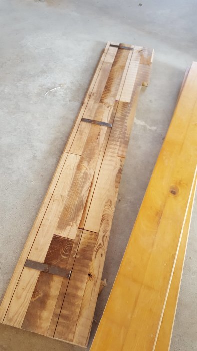 Uppskuret massivt ekgolv ligger på en betonggolv, synliga sågkanter och plankstumpar.