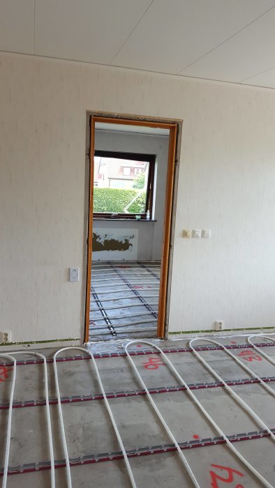 Nyinstallerade golvvärmeslingor på ett betonggolv i ett rum med synlig dörröppning.