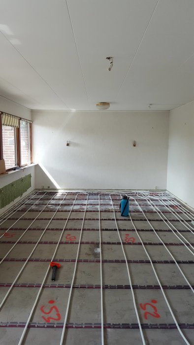 Installation av golvvärmeslingor på isolerplattor i ett rum under renovering.