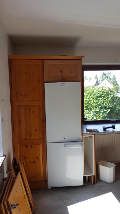 Gammalt kök med träskåp och vit kyl innan renovering.