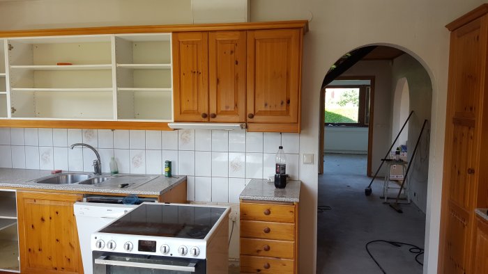 Ett omodernt, tomt kök med öppna träskåp och kakel innan renovering.