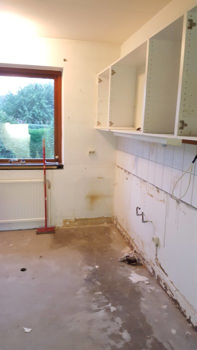 Tomt kök under renovering med borttagen inredning och synliga vägg- och golvskador.