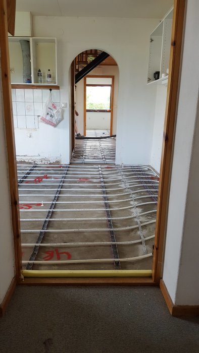 Renoveringsprojekt med avlägsnat golv och synlig golvvärmeinstallation i ett tomt kök.