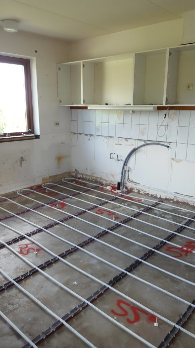 Renoveringsarbete i kök med öppna väggskåp och installerade golvvärmeslingor på betonggolv.