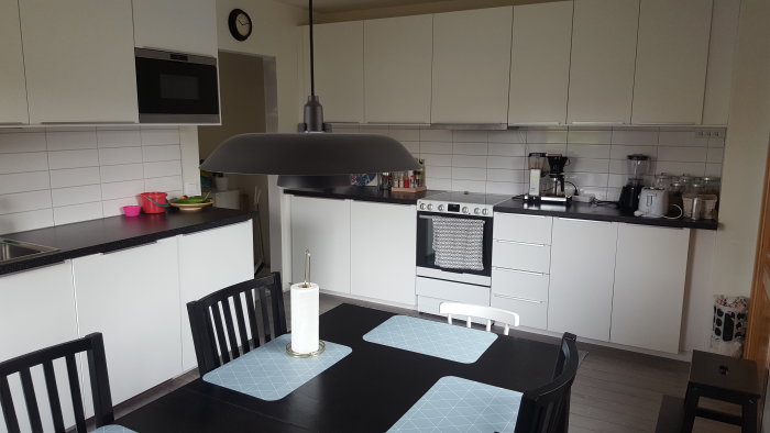 Renoverat modernt kök med vita skåp, svarta bänkskivor och matbord med stolar.