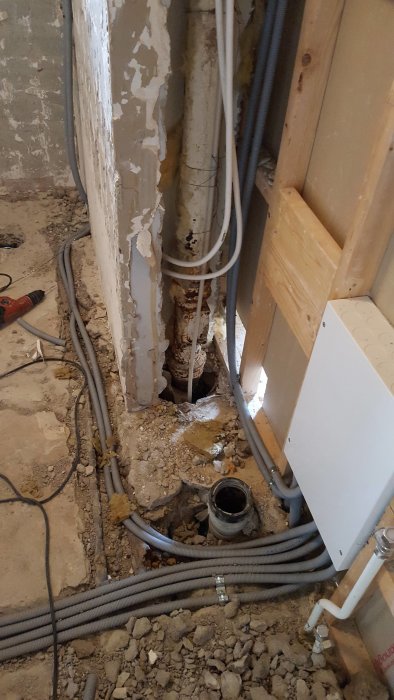 Rivningsfas av badrum med exponerade rör och elektriska ledningar, betonggolv och väggytor.