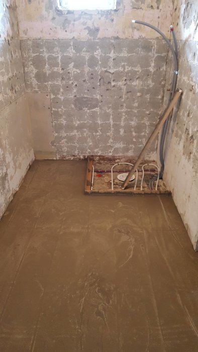 Renoveringsfas av ett badrum med avtagna väggplattor och pågående golvinstallation.