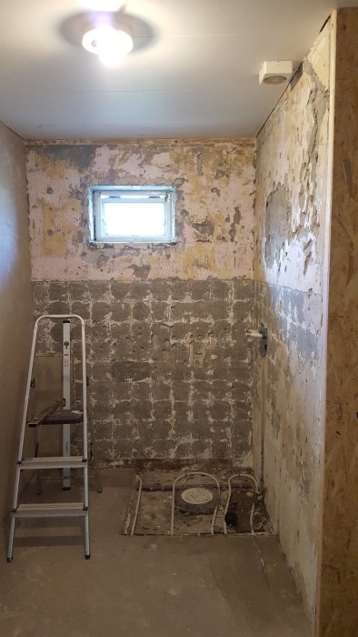 Renoveringsprojekt i badrum, väggar och golv är avskalade, stege och installationsdelar syns.