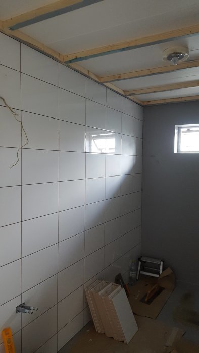 Renoveringsarbete i badrum med halvlagda vita kakelväggar och byggmaterial på golvet.