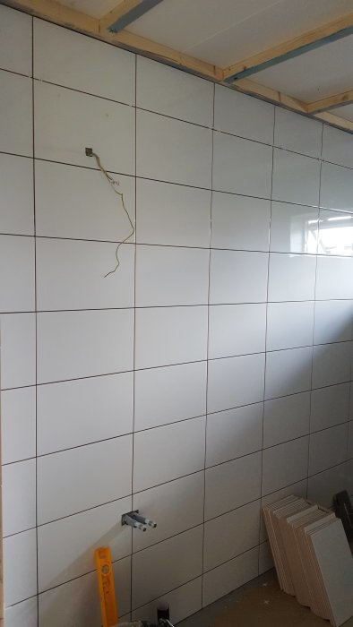 Omonterat badrum med vit kakelvägg, synliga elledningar och byggmaterial på golvet.