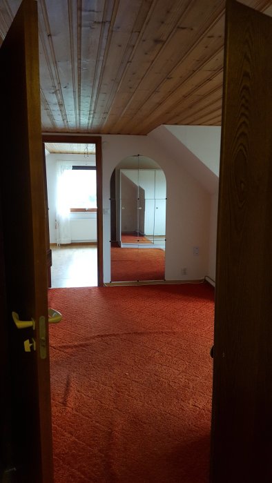 Ovanvåning före renovering med orange heltäckningsmatta och obehandlat trästak.