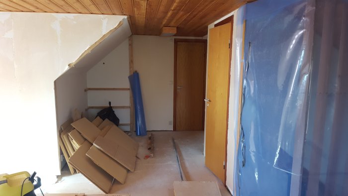 Renoveringsfas av en ovanvåning med synliga byggmaterial och plastskydd.