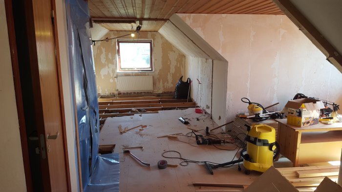 Ovanvåning under renovering med borttagna golvbrädor, verktyg och renoveringsbråte.