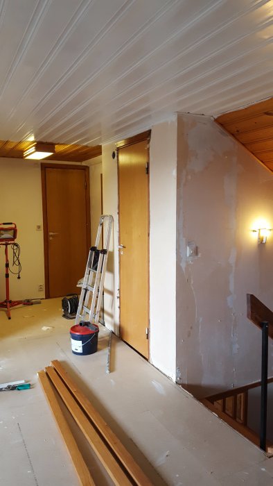 Renoveringsarbete på en ovanvåning med spacklade väggar, stegar och brädor på golvet.