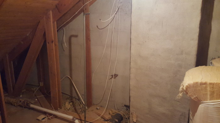 Oavslutat ovanvåningsrum med träreglar, betongvägg och elledningar.