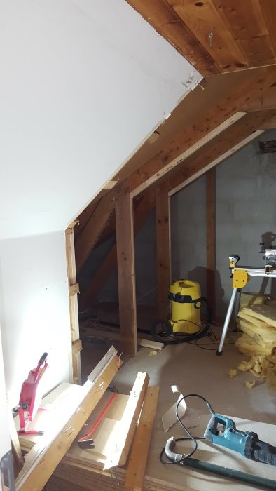 Underrenovering av vind med träreglar, snedtak, isolering och byggverktyg.