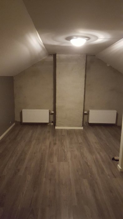 Renoverad ovanvåning med trägolv, sluttande tak, vita väggar och två element.