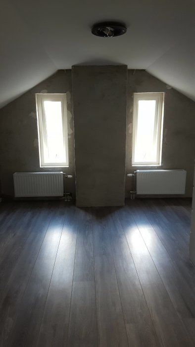 Ovanvåning under renovering med oavslutade väggar, två fönster och mörkt trägolv.
