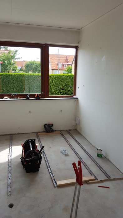 Rum under renovering med verktyg på golv, osynlig golvvärme, och stort fönster med utsikt.